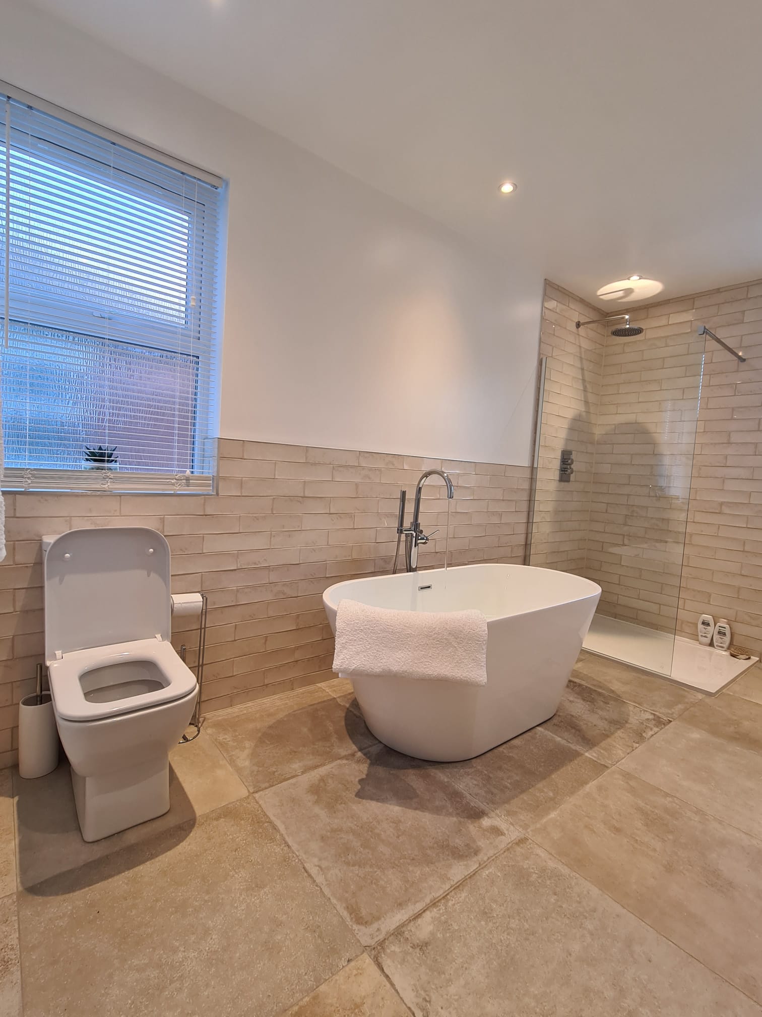 Bathroom with a freestanding bath, walk-in shower and warm stone-effect tiles